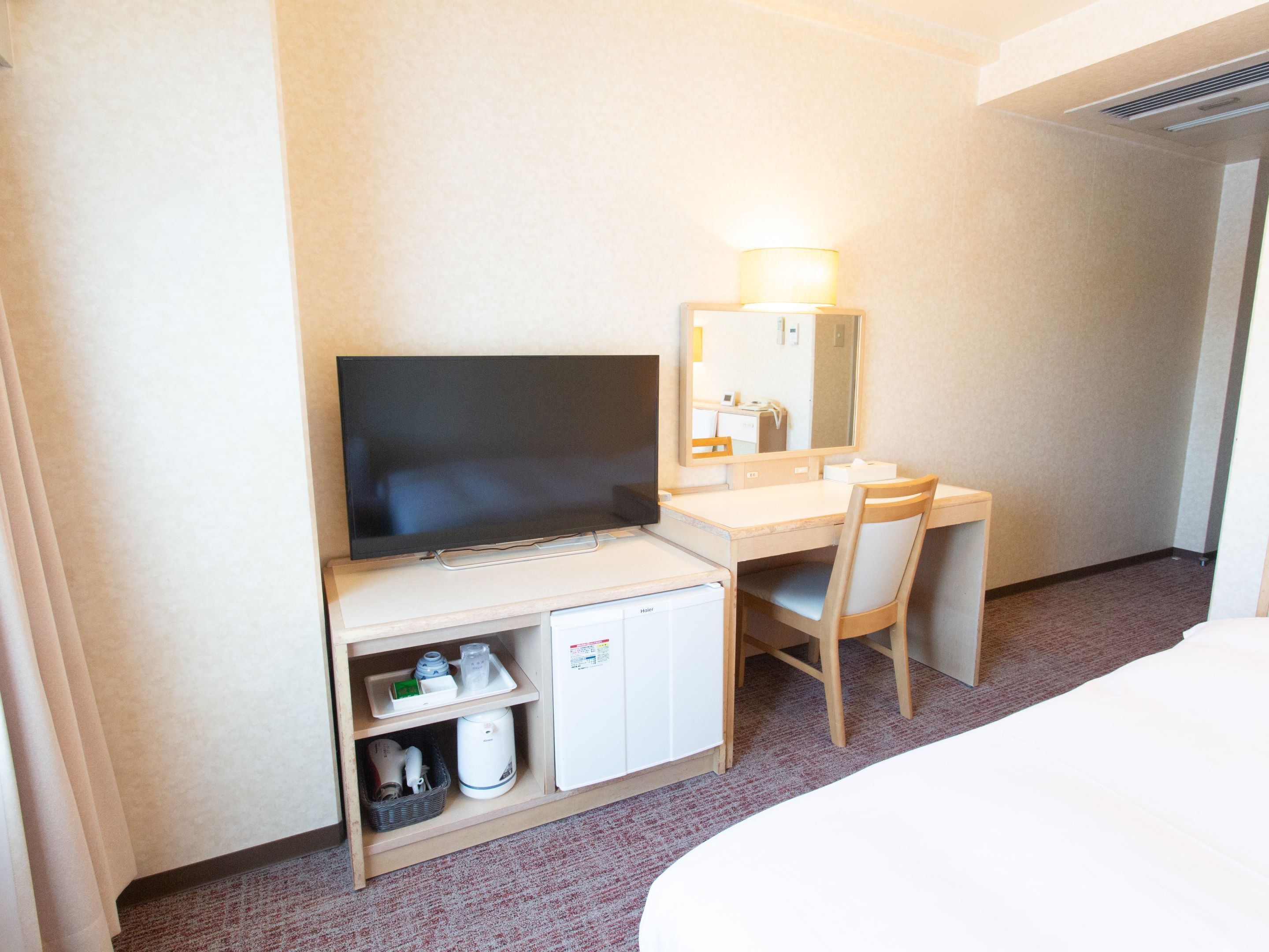 Une chambre d’hôtel équipée d’un téléviseur à écran plat, d’un bureau, d’une chaise, d’un miroir, d’un mini-réfrigérateur et d’un lit.
