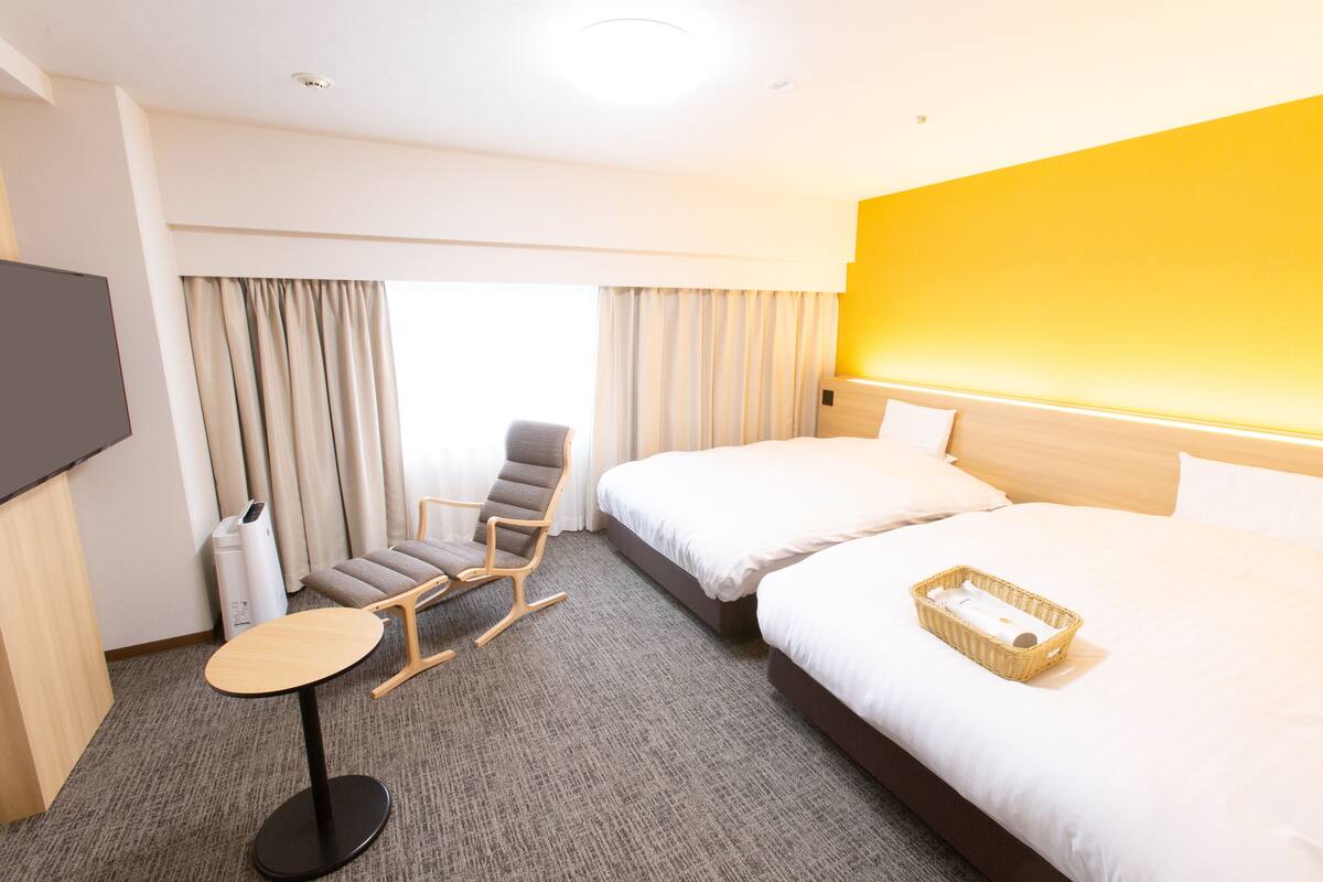 A hotel room with two beds, a chair, a small table, and a TV.