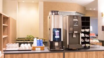 A counter with two beverage dispensers, a basket of bottled water, and a shelf with napkins and tissues.