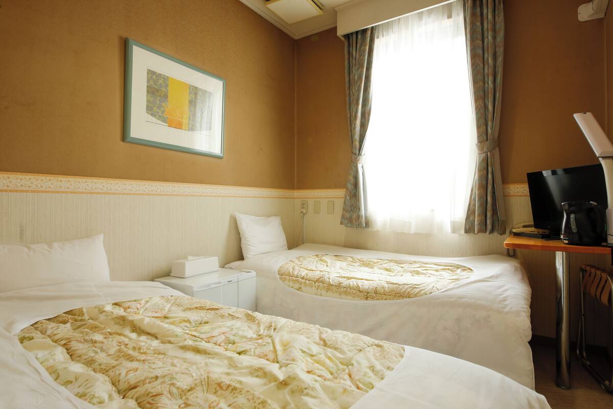 Une chambre d’hôtel avec deux lits, un bureau, une télévision et une fenêtre avec des rideaux.