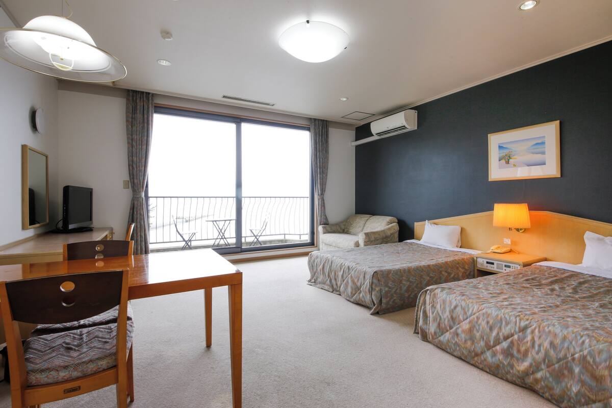Une chambre d’hôtel avec deux lits, un bureau, une chaise, une télévision et un balcon avec vue.