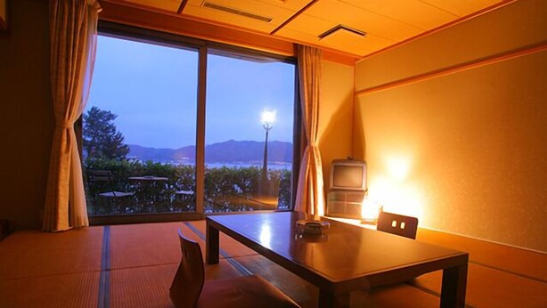 A room with tatami flooring, a low table, and a view of a mountain and water at dusk. - AMANOHASHIDATESOU (Miyazu)