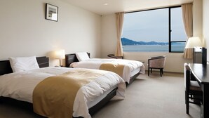 Ein Hotelzimmer mit zwei Betten, einem Schreibtisch, einem Stuhl, einer Lampe und einem großen Fenster mit Meerblick.