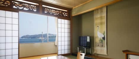 A traditional Japanese room with tatami flooring, a low wooden table, a television, and a painting of a crane.