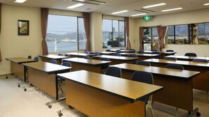 Ein Klassenzimmer mit Schreibtischen, Stühlen und großen Fenstern, durch die man eine Brücke und Hügel sehen kann.