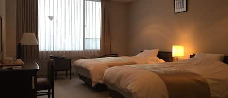 A hotel room with two beds, a desk, a chair, and a window with curtains.