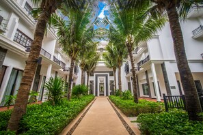 A corridor lined with palm trees and lush greenery, leading to a central entrance with a decorative archway. - Lotus Blanc Hotel (Siem Reap)
