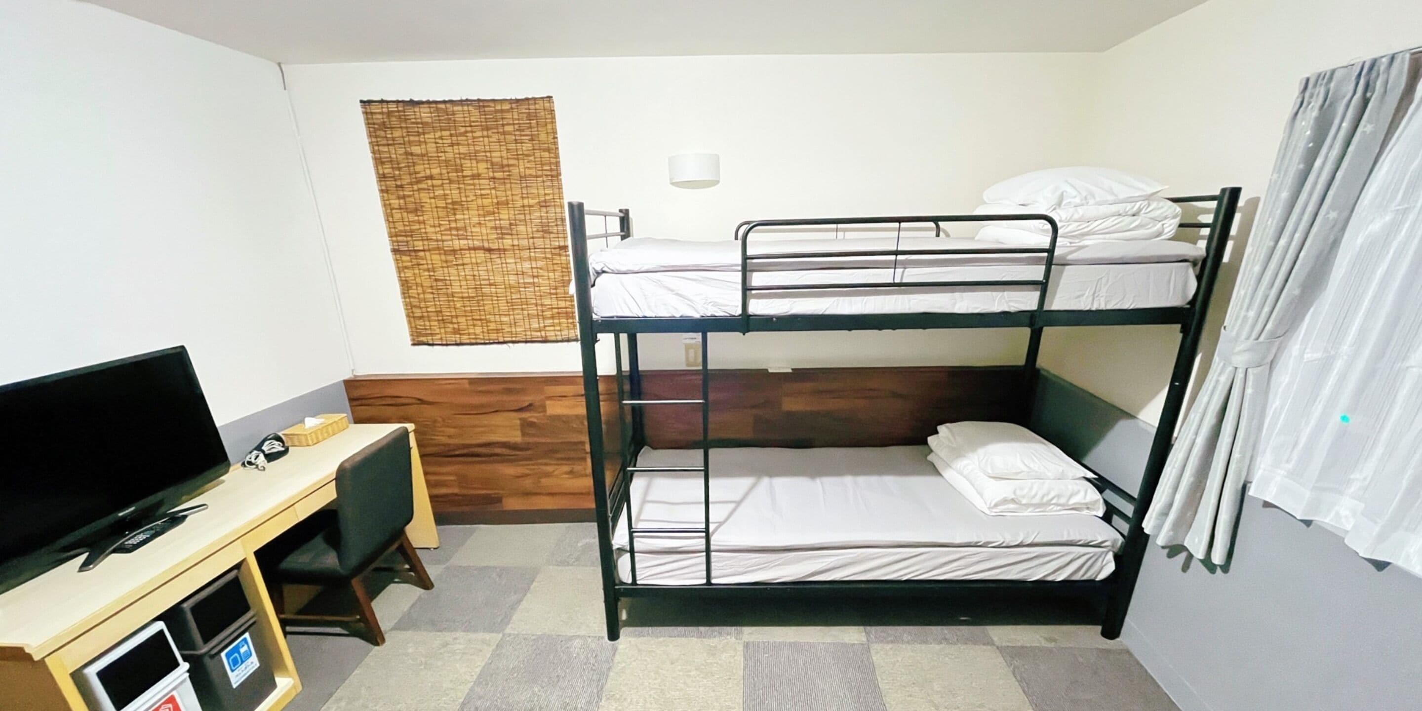 A bunk bed room with a desk, television, and a window with curtains.
