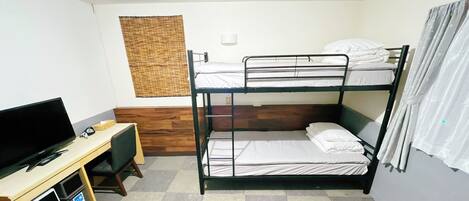 A bunk bed room with a desk, television, and a window with curtains.