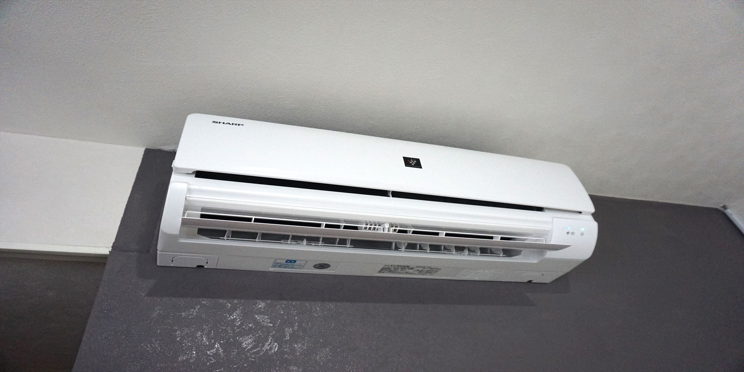 Un equipo de aire acondicionado blanco montado en una pared de una habitación con suelo gris y paredes blancas.