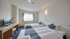 Et hotelværelse med to senge, et skrivebord med computer og et vindue med gardiner.