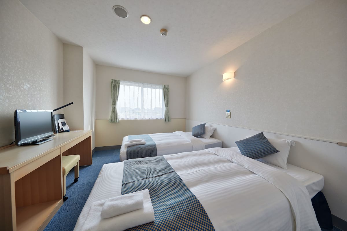A hotel room with two beds, a desk with a computer, and a window with curtains.