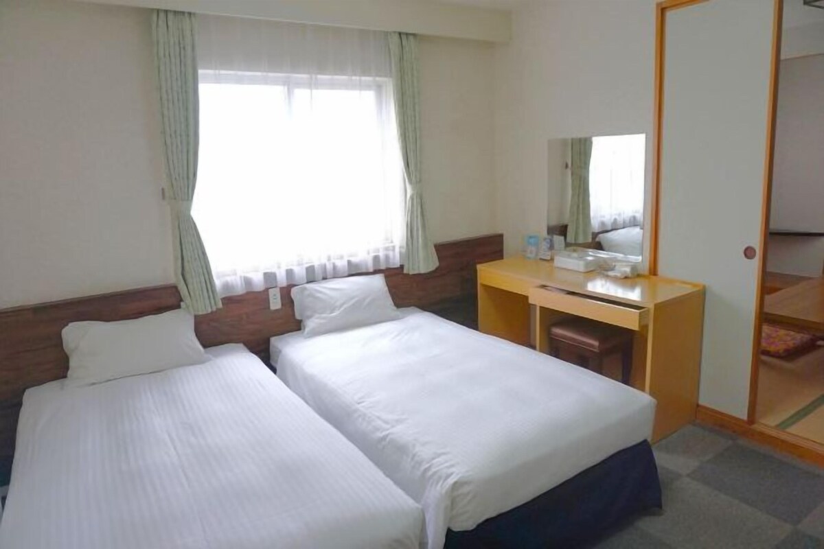 Una habitación de hotel con dos camas individuales, un escritorio de madera, un espejo y una ventana con cortinas.