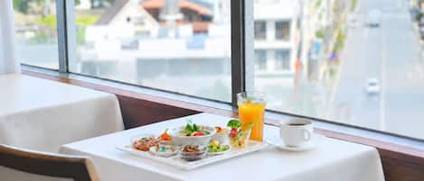 A breakfast setting with a table set for two, a glass of orange juice, a cup of coffee, and a variety of small dishes with food.