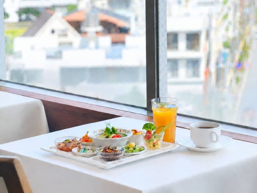 Desayuno preparado para dos personas, con una mesa, vaso de jugo de naranja, taza de café y varios pequeños platos con comida.