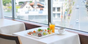 Une table mise pour le petit-déjeuner, avec une nappe pour deux personnes, un verre de jus d’orange, une tasse de café et une variété de petits plats contenant différents aliments.