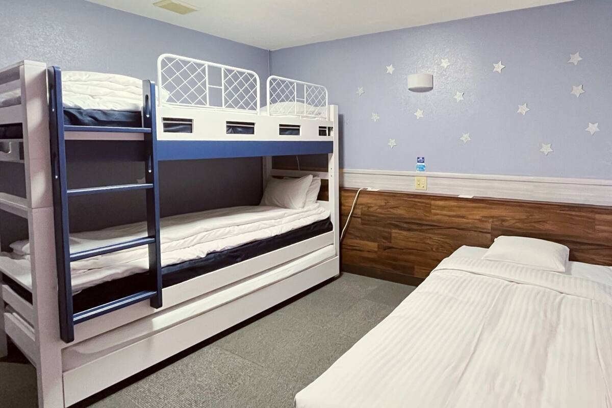 A room with bunk beds, a single bed, a wooden headboard, and star decals on the wall.
