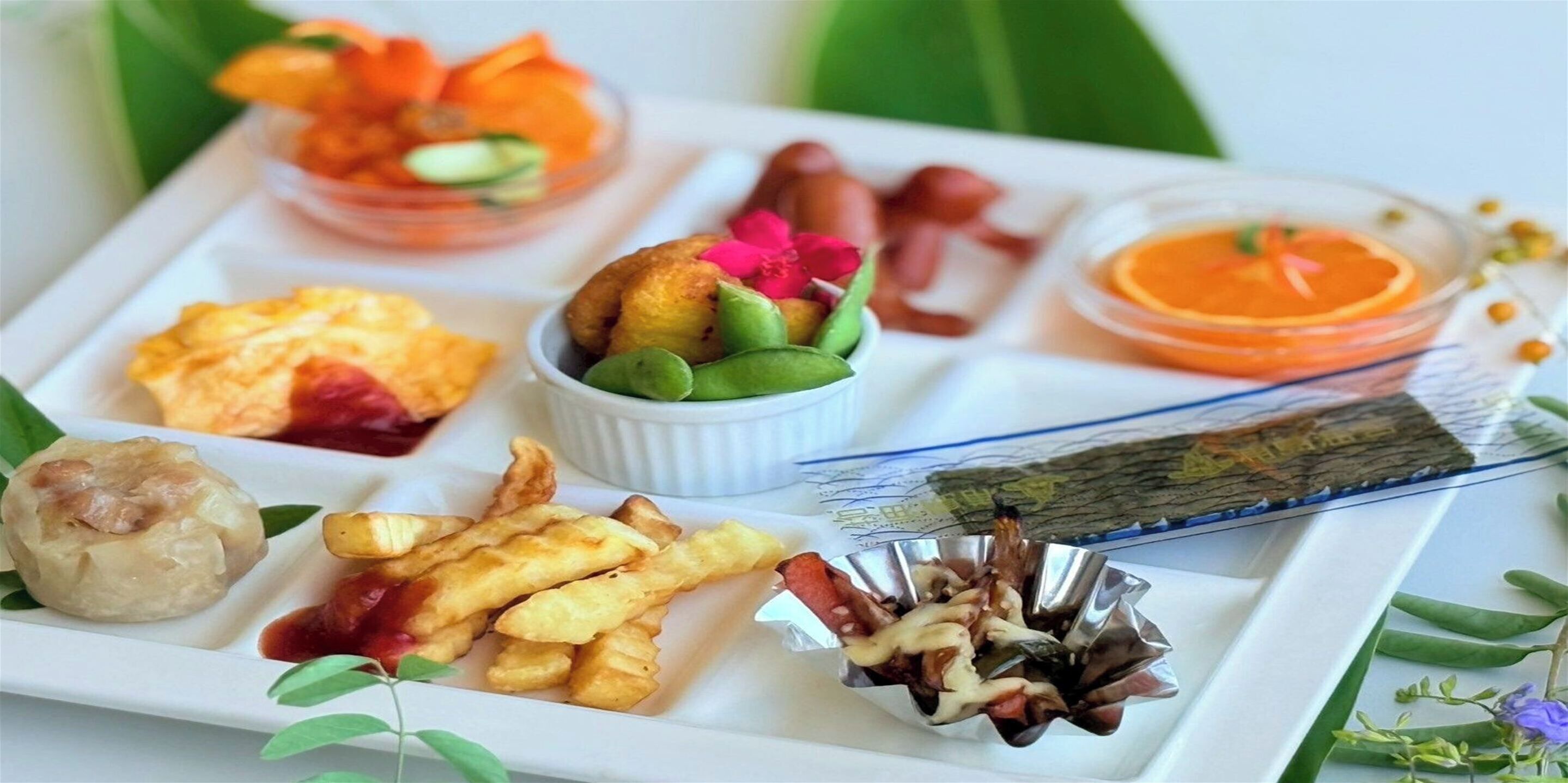 Una variedad de platillos en una bandeja, incluyendo dumplings, frituras y un tazón de fruta.