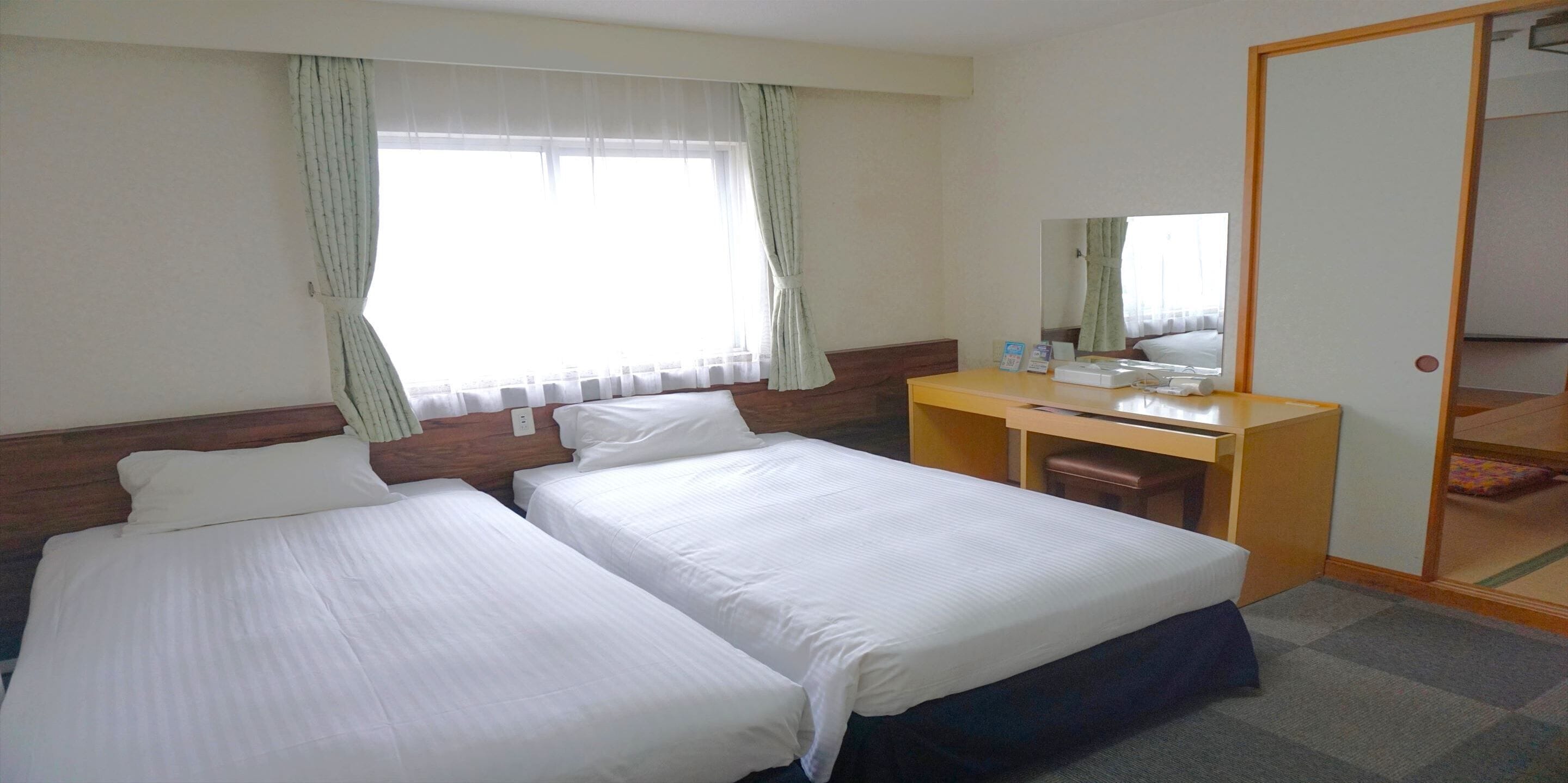 A hotel room with two beds, a desk, a chair, and a wardrobe.