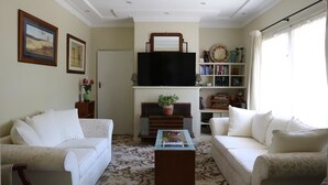 A living room with two white sofas, a coffee table, a fireplace, a television, and a bookshelf. - The Evergreen B&B (Braddon)