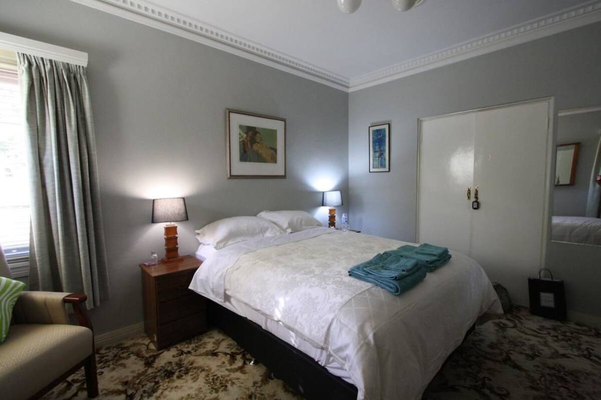 Una habitación de hotel con cama, mesita de noche con lámparas, una silla y un armario.