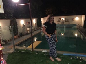 A person standing by a swimming pool at night.