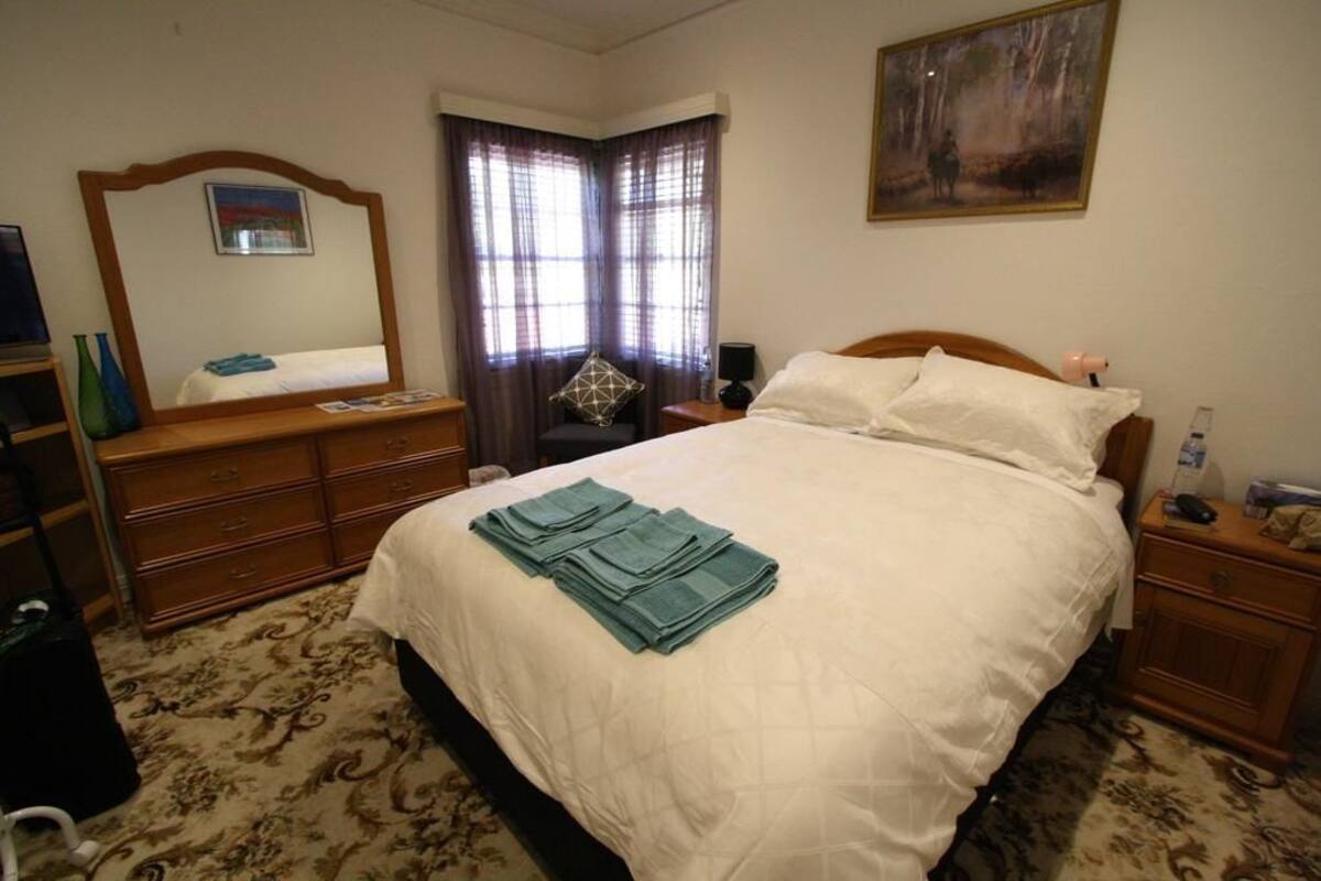 Un dormitorio con cama, cómoda, mesita de noche, espejo y ventana con cortinas.