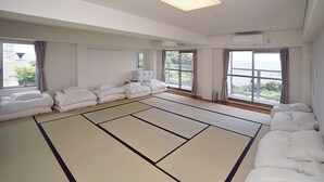 A room with tatami mats, white bedding, and large windows with curtains.