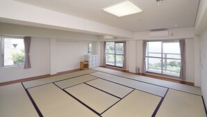 A spacious room with tatami mats, large windows, and a small wooden cabinet.
