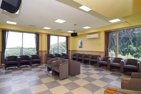 A hotel lobby with checkered flooring, multiple seating areas, large windows with curtains, a mounted television, and an air conditioning unit on the wall.