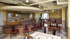 A restaurant with a curved counter, wooden chairs with red cushions, and a checkered floor.