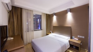 Een hotelkamer met een bed, nachtkastje, lamp en een raam met gordijnen.