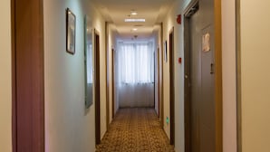 Een hotelgang met een kamergestreept tapijt, deuren en ingelijste foto's aan de wanden.