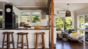Una cocina con taburetes de madera, un reloj y una ventana con vistas a follaje.
