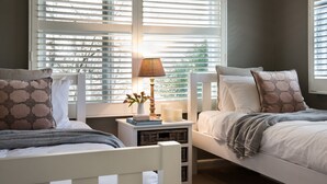Un dormitorio con dos camas, una mesita de noche con lámpara y una ventana con persianas.