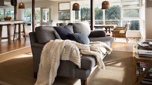 Una sala de estar acogedora con un sofá gris, una manta tejida y una silla de mimbre.