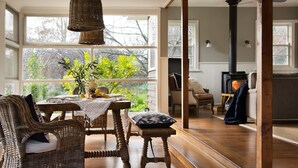Una sala de estar acogedora con un ventanal grande, muebles de mimbre, una mesa con un florero y una chimenea.