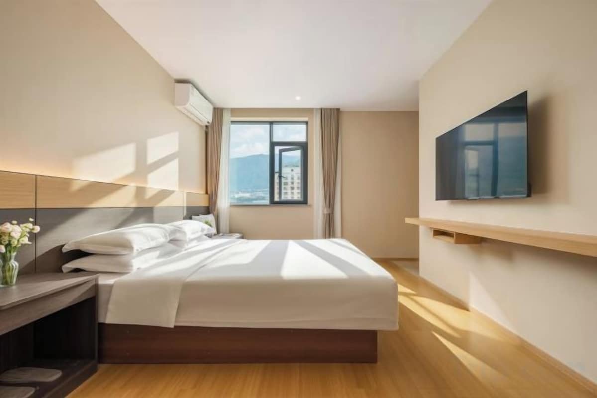 A hotel room with a bed, a TV, a window with a city view, and a desk with a lamp.