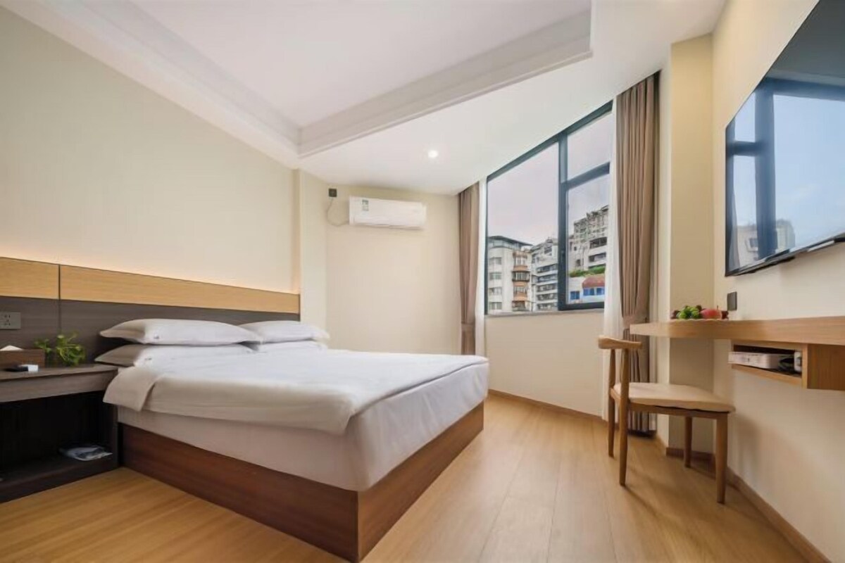 A modern hotel room with a bed, bedside table, and a large window.