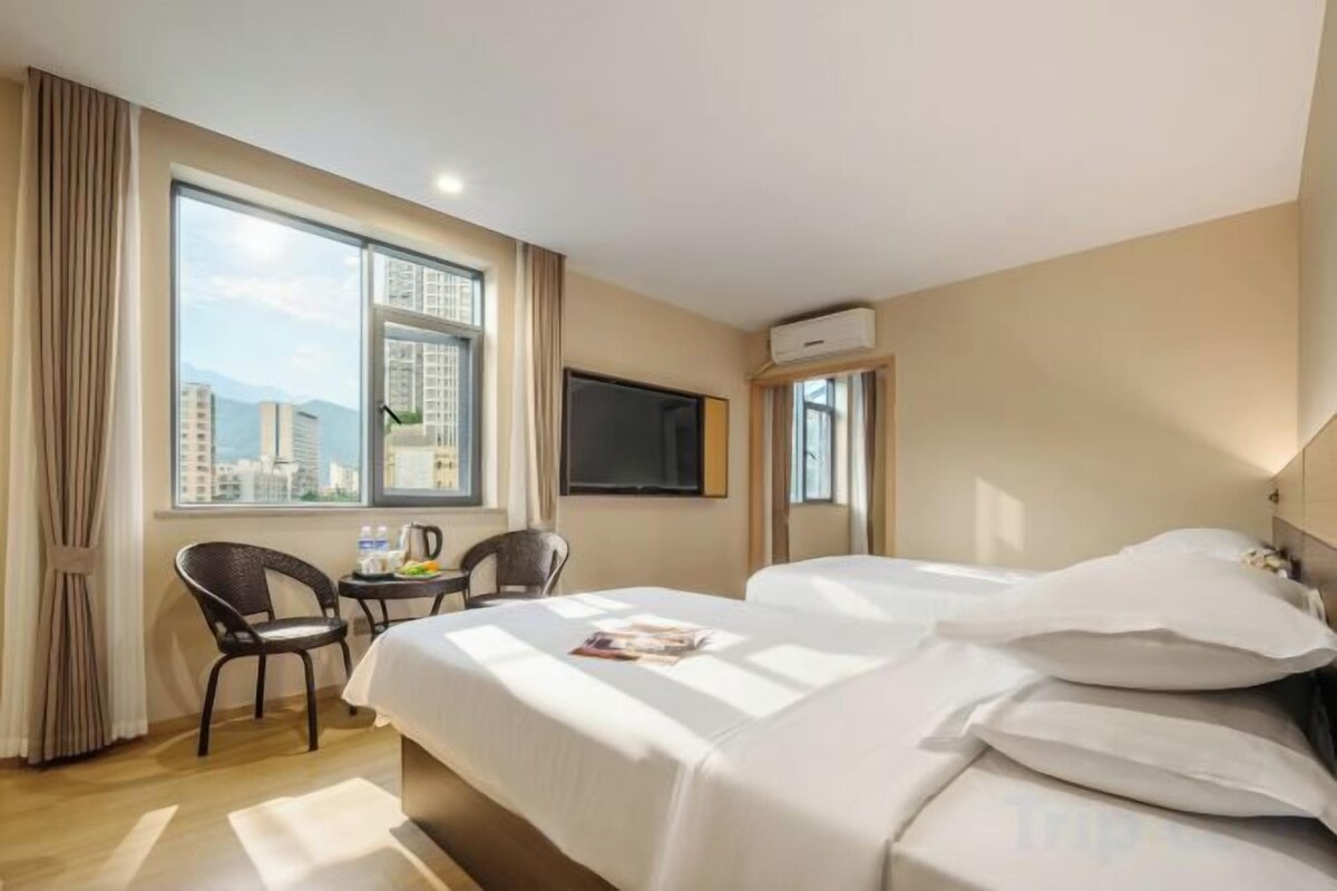 A hotel room with a bed, a TV, a window with a city view, and a small table with chairs.
