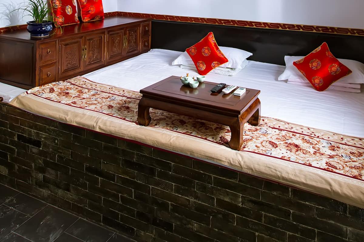 Ein traditionell eingerichteter Raum mit einem Bett, einem kleinen Tisch, einem Stuhl und einem an der Wand befestigten Schrank.