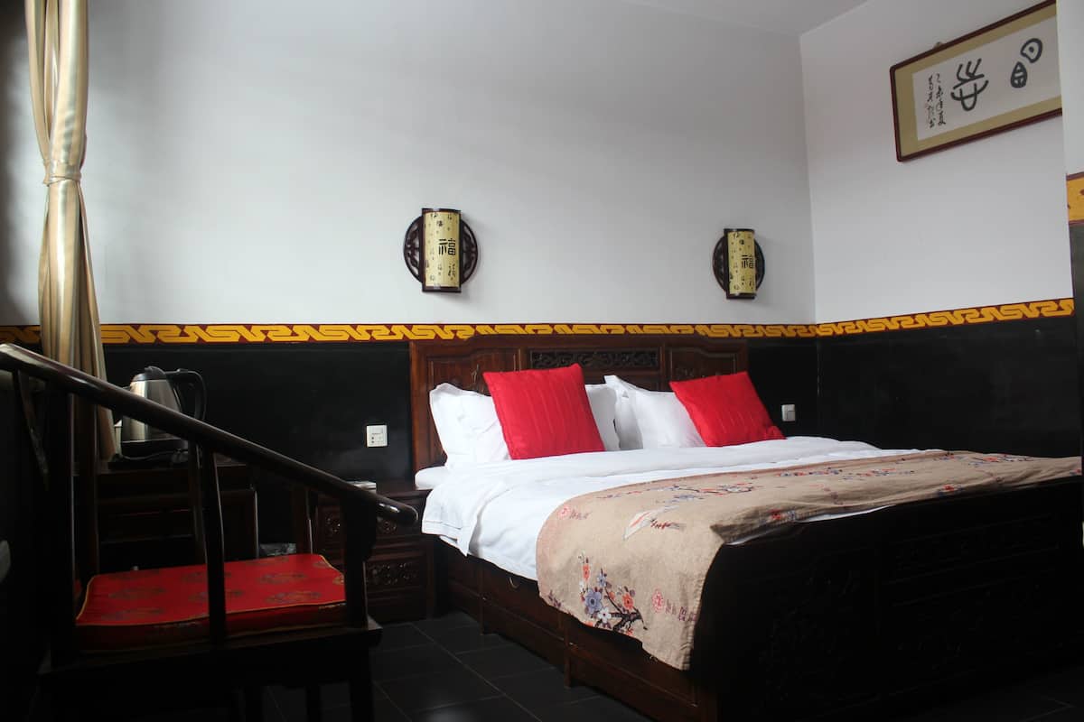 Ein Schlafzimmer mit einem hölzernen Bett, roten und weißen Kissen, einer blumigen Tagesdecke, einem Nachttisch aus Holz und einer Treppe.