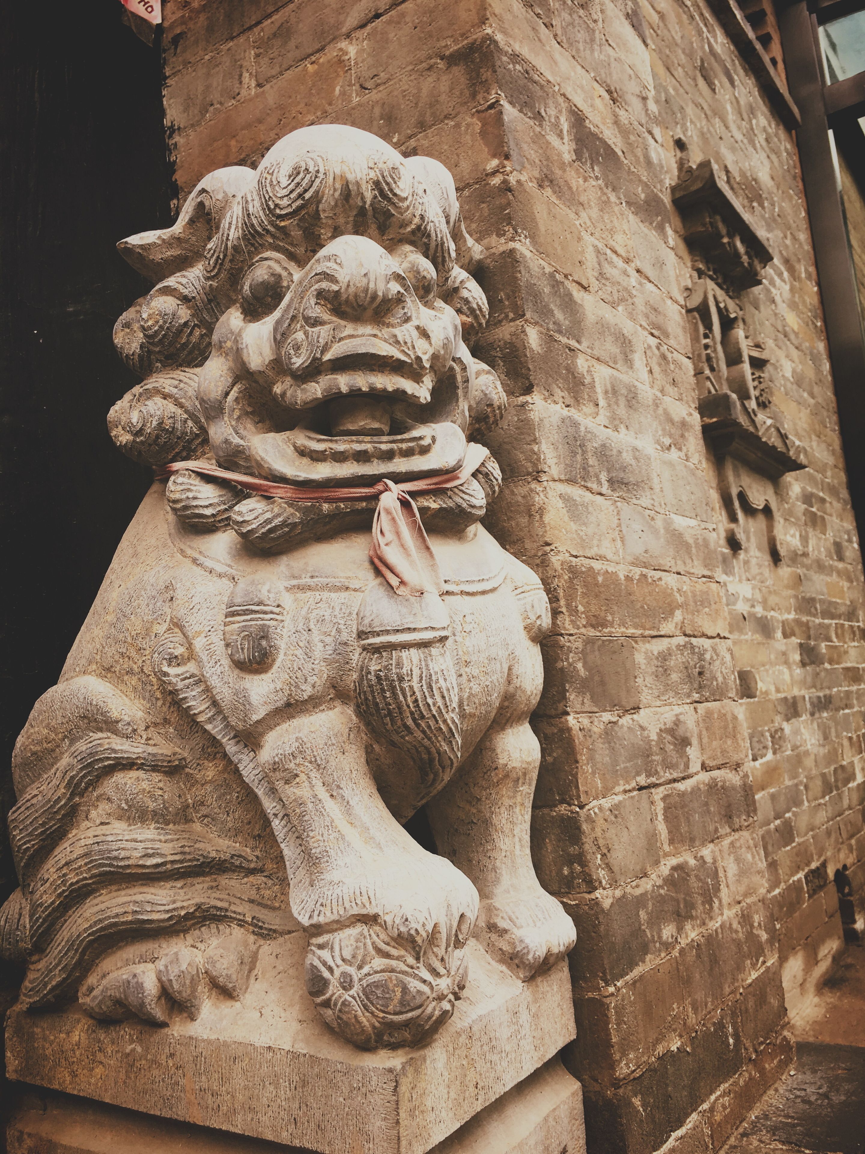 A stone lion sculpture attached to a brick wall.