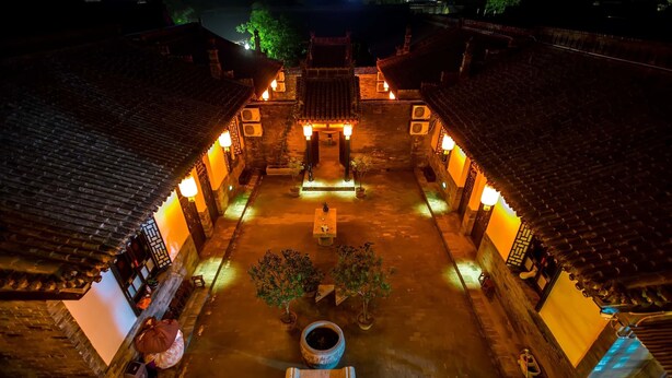 A traditional courtyard with tiled roofs and lanterns, surrounded by buildings with wooden doors and windows.