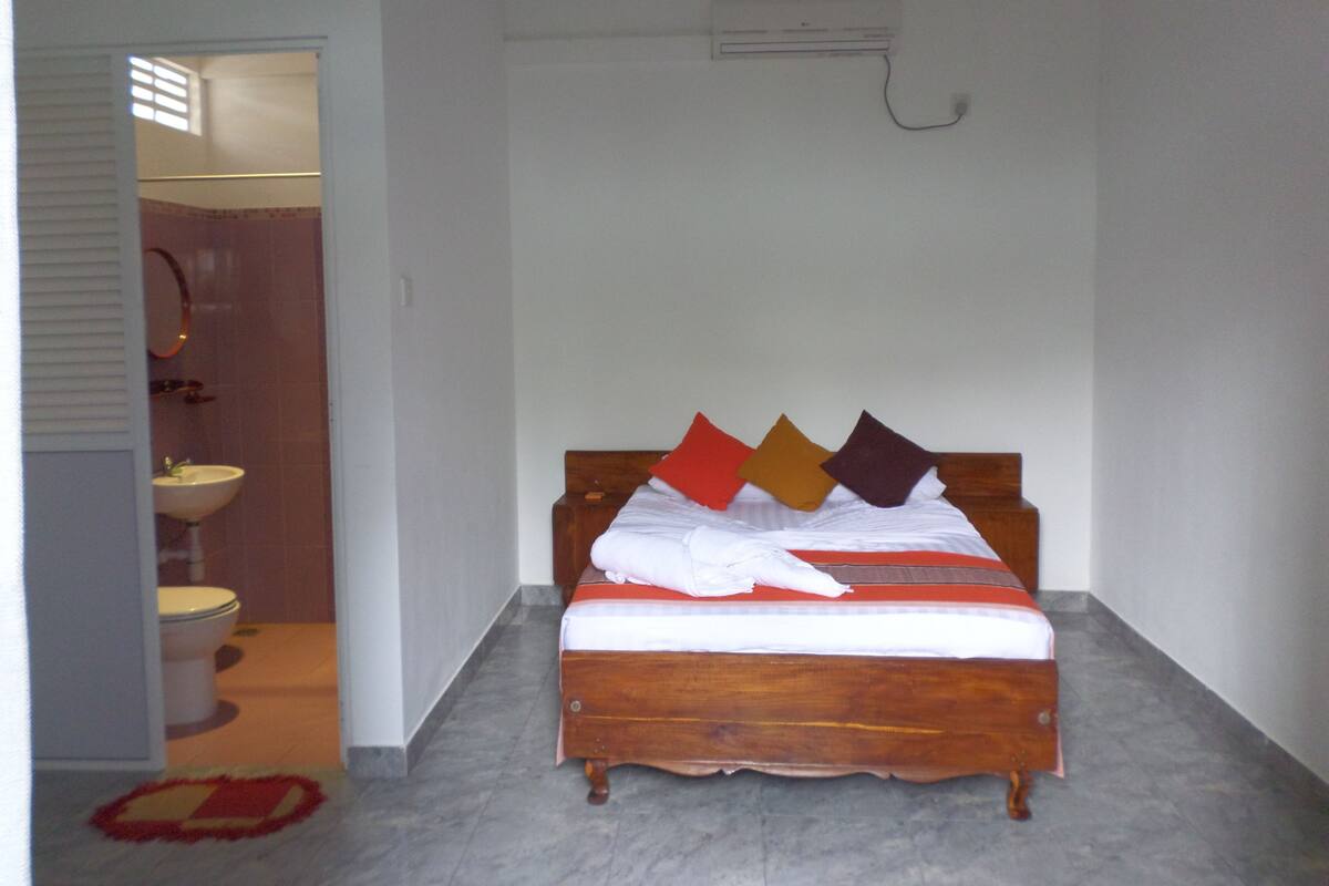 A bedroom with a wooden bed, a white wall, and an air conditioning unit.