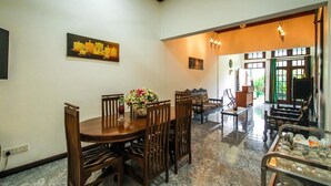 Un coin repas avec une table ronde, des chaises en bois et un vase de fleurs. On aperçoit un canapé et une petite table avec une lampe à l’arrière-plan.