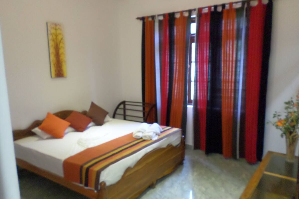 A bedroom with a bed, pillows, a wooden headboard, a glass table, and curtains.
