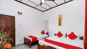 Une chambre d’hôtel avec deux lits en bois, du linge de lit blanc, des touches de couleur rouge, un ventilateur de plafond et une porte en bois.
