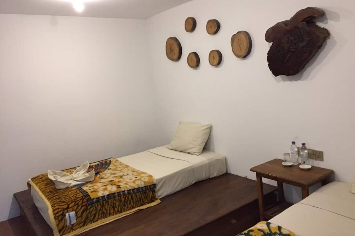 Ett litet, enkelt rum med en säng, ett litet bord med flaskor på och en vägg som är dekorerad med träskivor och en utskuren trädetalj.
