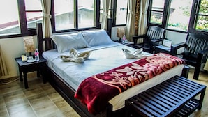 A hotel room with a bed, a bedside table with a lamp, a chair, and a desk with a chair.